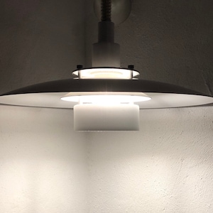 May include: A white ceiling light fixture with a circular shade and a white cylindrical diffuser. The light is on and casting a warm glow.