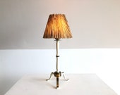 Vintage art deco three-legged table lamp in brass with white painted metal details in gorgeous design and pleated shade with straw