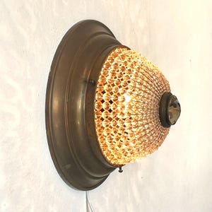 May include: A brass wall sconce with a crystal bead shade. The shade is a dome shape and has a large crystal in the center.