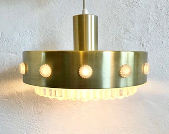 Może przedstawiać: Złota metalowa lampa wisząca z okrągłą podstawą i przezroczystymi szklanymi panelami. Lampa ma rząd małych, okrągłych, białych świateł wokół krawędzi podstawy.