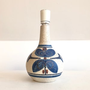 Könnte beinhalten: Eine weiße Keramik-Lampenbasis mit einem blauen und braunen Blumendesign. Die Lampenbasis hat einen weißen Schirm.