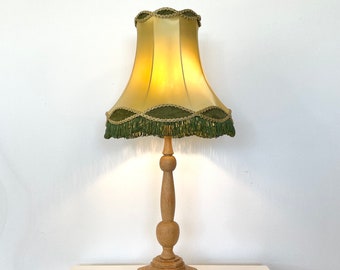 May include: A wooden table lamp with a green and gold lampshade. The lampshade has a scalloped edge and a fringe trim.