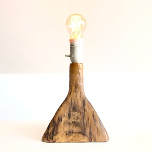 Könnte beinhalten: Eine Keramik-Tischlampe mit einer warm leuchtenden Glühbirne. Der Lampenfuß hat eine einzigartige, organische Form mit braunen und beigen Farbtönen. Die Glühbirne ist im klassischen Edison-Stil gehalten.