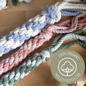 May include: Close-up of several braided cotton rope toys in pastel colors: blue and white, pink, and green. The toys are labeled "100% Organic Recycled Cotton". These toys are likely for pets.