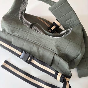 Puede incluir: Bolso de hombro acolchado verde oliva con una correa a juego y una correa ajustable a rayas negras y beige. El bolso tiene un bolsillo frontal y una hebilla de pl&aacute;stico negro. El forro interior tiene un estampado de cuadros.
