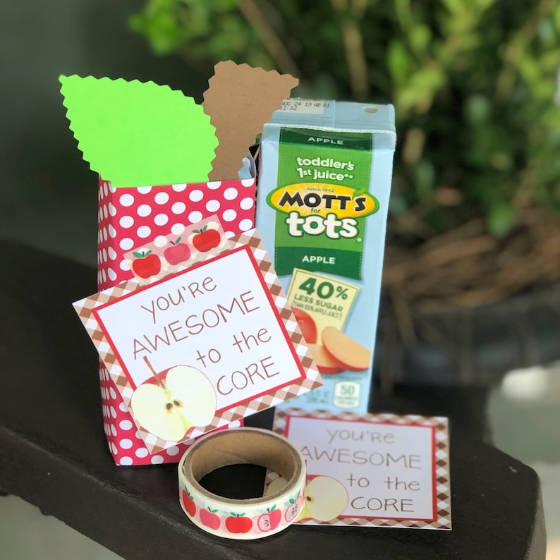 May include: A red and white polka dot gift bag with a green leaf on top. The bag contains a small juice box with the words "Mott's for tots" on it. There is a small card attached to the bag that says "You're Awesome to the Core" with a red apple graphic. There is also a roll of washi tape with red apples on it.