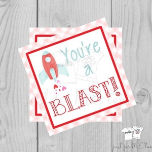 May include: A red and white Valentine's Day card with a rocket ship and a t-shirt. The card says "You're a Blast!"
