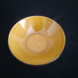 以下が含まれることがあります： 濃い茶色の縁取りのある黄色のセラミックボウル。ボウルは空で、光沢のある仕上げになっています。