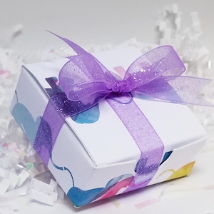 May include: A small white gift box with a purple ribbon and bow. The box has a colorful abstract design.