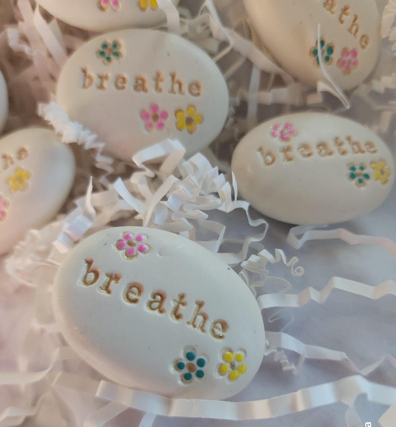 May include: White painted stones with the word "breathe" written on them. Each stone has colorful flowers painted on them.