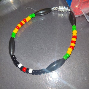 May include: A beaded bracelet with black, red, yellow, and green beads. The bracelet has a silver clasp and two black oval beads.