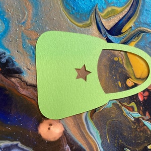 May include: A light green felt bag with a star cut out. The bag is on a colorful background with swirls of blue, green, yellow, and brown.