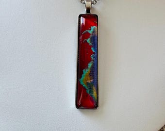 May include: A silver chain necklace with a rectangular pendant featuring abstract red, blue, green, and yellow paint swirls.