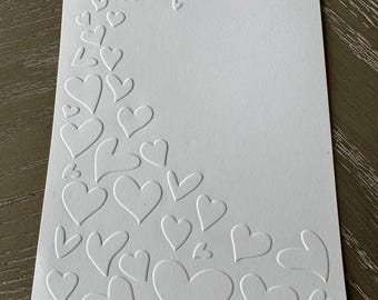 May include: White card with a border of embossed hearts. The hearts are of varying sizes and are arranged in a curved line.