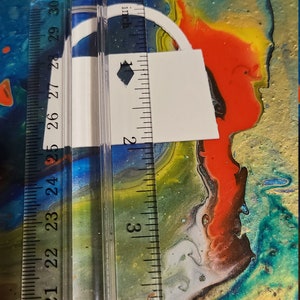 May include: A white paper lock shape with a black diamond in the center, measured with a ruler in inches. The lock is approximately 2 inches tall and 1.5 inches wide.