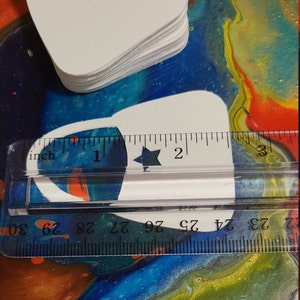 May include: A stack of white paper bags with a star cut out. The bags are approximately 2 inches wide and 3 inches tall. A ruler is used to show the size of the bags.