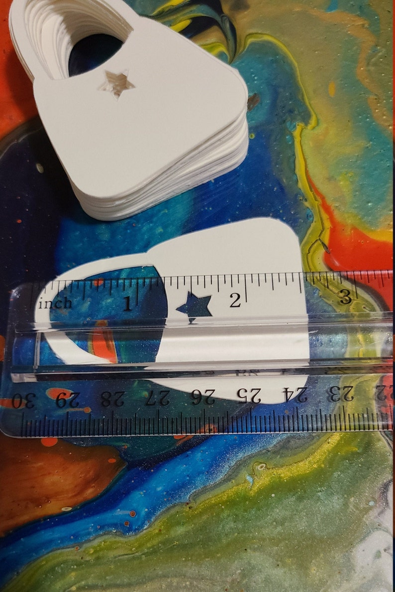 May include: A stack of white paper bags with a star cut out. The bags are approximately 2 inches wide and 3 inches tall. A ruler is used to show the size of the bags.