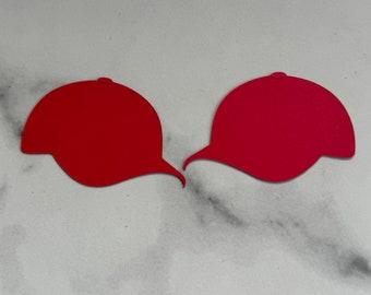 May include: Two red paper baseball caps, one facing left and the other facing right, on a white marble background.