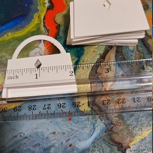 May include: A stack of white paper cutouts shaped like arches with a diamond cutout in the center. The cutouts are measured against a ruler with inch markings.
