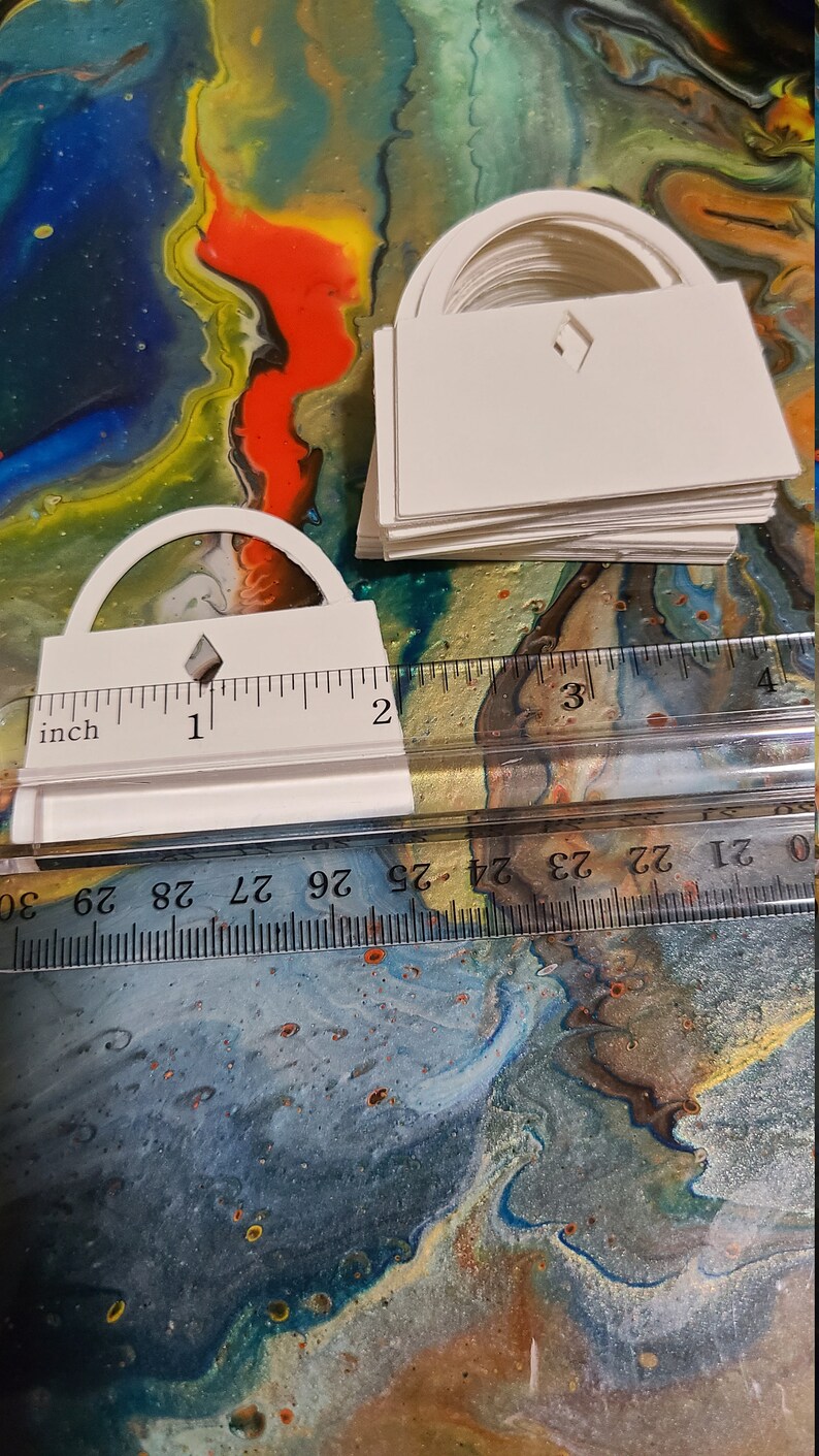 May include: A stack of white paper cutouts shaped like arches with a diamond cutout in the center. The cutouts are measured against a ruler with inch markings.