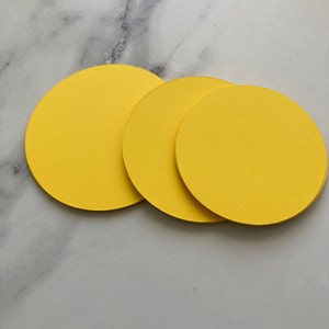 May include: Three yellow round paper coasters. The coasters are stacked on top of each other.