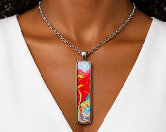 May include: A silver-toned necklace featuring a long, rectangular pendant with a vibrant, multi-colored marbled pattern. The pendant displays swirling hues of bright red, yellow, white, and blue, suspended from a simple silver-toned chain link necklace.