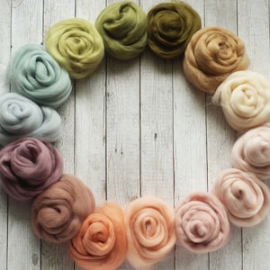 Könnte beinhalten: Ein Kreis aus bunten Wollrohlingen in Grüntönen, Blau, Rosa und Braun. Die Rohlinge sind in einem Farbverlauf angeordnet, beginnend mit Grün und endend mit Braun.