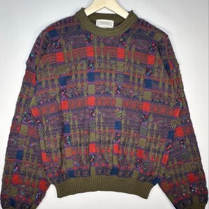 May include: A long-sleeve crew neck jumper featuring a complex multi-coloured woven pattern in shades of olive green, red, blue, and purple. The garment has a solid olive green ribbed knit collar, cuffs, and hem, with a label reading Expressions.