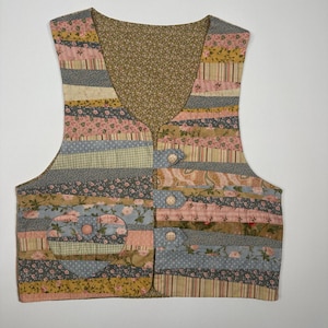 Op de afbeelding: Een patchwork vest met diverse bloemen- en streepmotieven in roze, blauw, geel en grijs. Het vest heeft een V-hals, een knoopsluiting en twee zakken. De binnenvoering is een effen bruin bloemenpatroon.