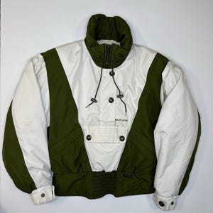 May include: A vintage ski jacket in white and olive green. The jacket features a high collar, a drawstring, and the word "sunice" printed on the front. The jacket has a ribbed waist and cuffs.