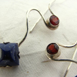 Puede incluir: Un par de pendientes de plata con una piedra de lapisl&aacute;zuli azul y una piedra de granate roja.