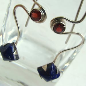 Puede incluir: Un par de pendientes de plata con una piedra de granate roja y una piedra de lapisl&aacute;zuli azul. Los pendientes tienen un dise&ntilde;o &uacute;nico y abstracto.