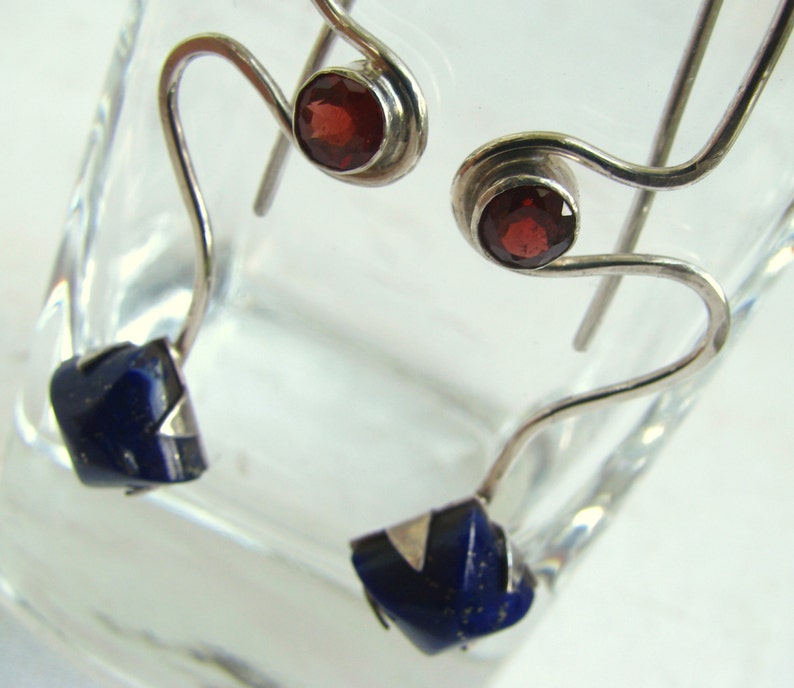 Puede incluir: Un par de pendientes de plata con una piedra de granate roja y una piedra de lapisl&aacute;zuli azul. Los pendientes tienen un dise&ntilde;o &uacute;nico y abstracto.