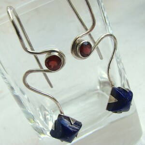 Puede incluir: Un par de pendientes de plata con piedras preciosas rojas y azules. Los pendientes est&aacute;n hechos de alambre fino y retorcido y tienen un dise&ntilde;o &uacute;nico y moderno.