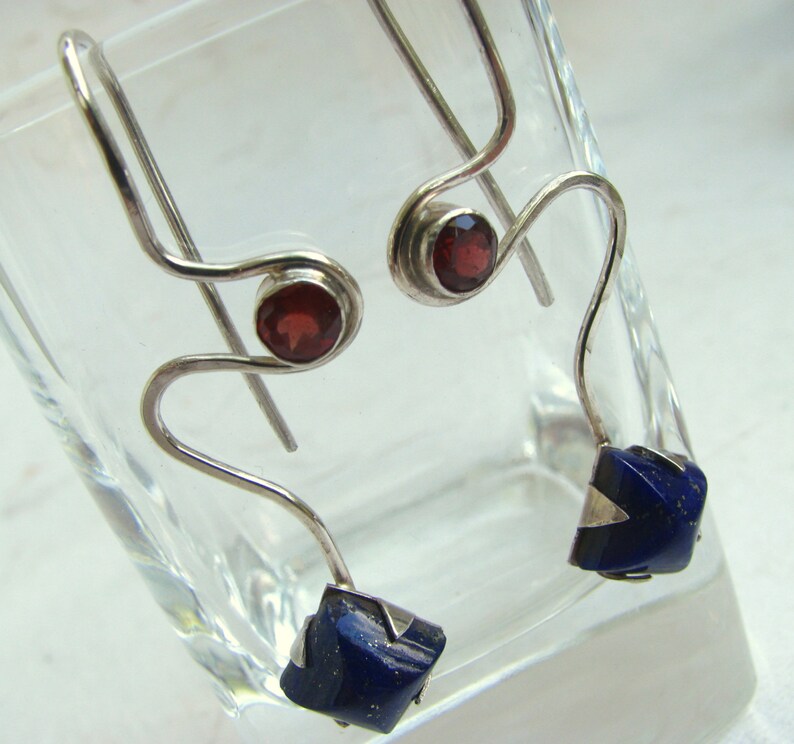 Puede incluir: Un par de pendientes de plata con piedras preciosas rojas y azules. Los pendientes est&aacute;n hechos de alambre fino y retorcido y tienen un dise&ntilde;o &uacute;nico y moderno.
