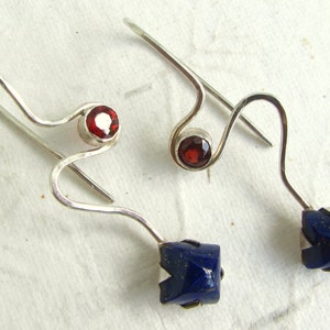 Puede incluir: Un par de pendientes de plata con una piedra preciosa roja y una piedra preciosa azul. Los pendientes est&aacute;n hechos de alambre retorcido y tienen un dise&ntilde;o simple.