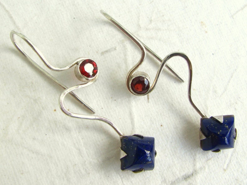 Puede incluir: Un par de pendientes de plata con una piedra preciosa roja y una piedra preciosa azul. Los pendientes est&aacute;n hechos de alambre retorcido y tienen un dise&ntilde;o simple.