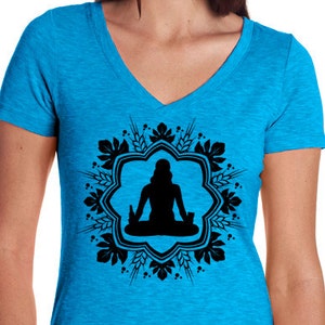 Puede incluir: Una camiseta de cuello en V azul turquesa con una silueta negra de una persona sentada en posición de loto dentro de un diseño circular de trigo y lúpulo. El diseño está centrado en la camiseta. La camiseta tiene un pequeño logotipo negro en la esquina inferior derecha que dice "hopcloth".