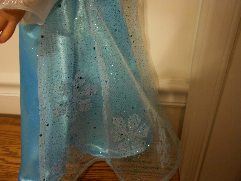 May include: A light blue dress with a sheer overlay and snowflake designs. The dress has a sparkly finish.