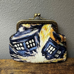 May include: A small, blue and yellow patterned coin purse with a brass clasp. The pattern features a stylized image of a building with windows.