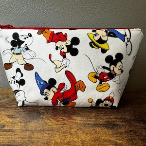May include: White zippered pouch with a red zipper pull. The pouch is decorated with a colourful print of various Mickey Mouse characters.