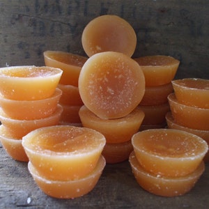 May include: A group of stacked orange wax melts in various sizes. The wax melts are arranged in a pyramid shape on a wooden surface.