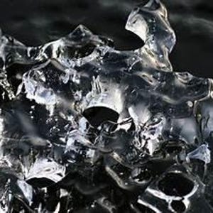 May include: Close-up of a translucent, irregularly shaped ice formation. The ice has a complex, textured surface with multiple peaks and valleys, reflecting light and creating a sparkling effect. The background is dark, providing contrast to the ice.