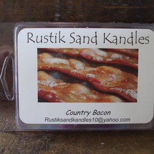 May include: A clear plastic container with a white label that reads "Rustik Sand Kandles" and "Country Bacon". The label also includes the email address "Rustiksandkandles10@yahoo.com". The image shows a close-up of crispy bacon.