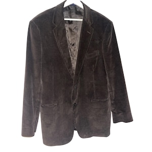 May include: A dark brown corduroy blazer with a two-button closure, notched lapels, and two front pockets. The jacket is hanging on a white hanger against a white background. The blazer has a classic, tailored design.