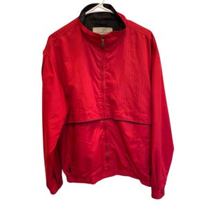 May include: A bright red jacket with a black collar and trim. The jacket has a full zipper closure and two pockets. The brand name "Peter Carey" is visible on the collar. The jacket is hanging on a white hanger.