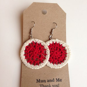 May include: A pair of crocheted earrings with a red and white design. The earrings are hanging on a brown card with the text "Mun and Me Thank you!"