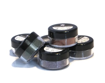 May include: Five small round jars of mineral eye shadow in various shades of green, brown, and gray. The jars are labeled "Nature Provides" and have a black lid.