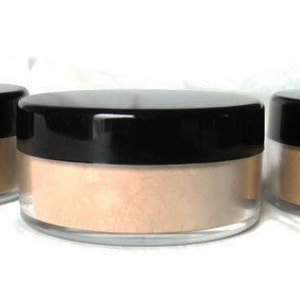May include: Three round, clear plastic cosmetic jars with black screw-on lids, each containing a different shade of loose face powder ranging from light beige to medium tan, arranged in a horizontal row against a plain white background.