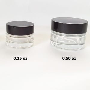 May include: Two glass jars with black lids. The smaller jar is labeled 0.25 oz and the larger jar is labeled 0.50 oz.